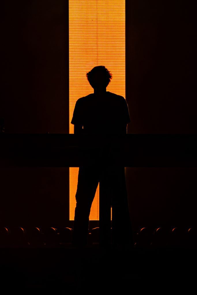 A silhouette stands in front of an orange sliver on an LED screen.